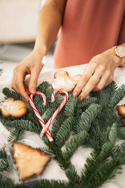 Kadın elleri ladin dallarına kırmızı lolipoplar koyar, kalp şekli oluşturur, yeni yıla hazırlık, tatil kurabiyeleri