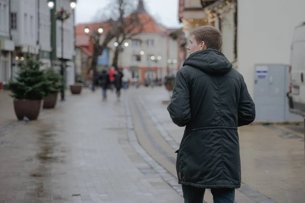 Bir turist gezisi, genç bir adam, siyah ceketli genç bir adam şehir caddesi boyunca yürüyor ve manzarayı inceliyor.