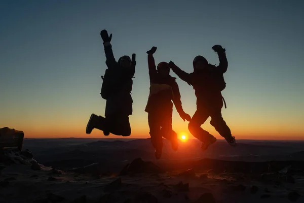 Kayak merkezi, üç insan silueti dağın tepesinde kırmızı bir günbatımında, neşeli bir yolculuk sırasında, neşeli bir arkadaş grubu