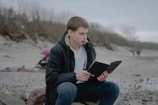 teenager sits on the beach reads a book, looks into a textbook. immersed in the study of the material