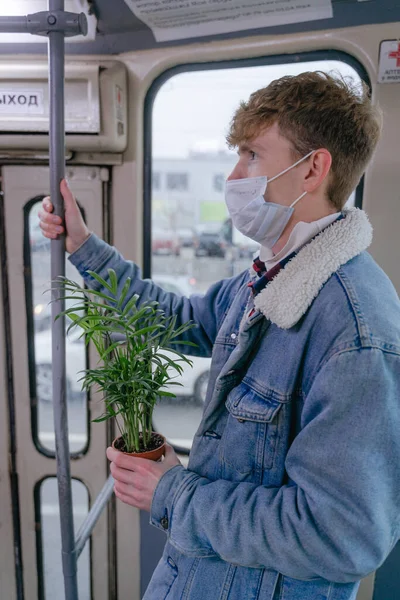 Toplu taşımadaki genç bir adam yüzünde tıbbi bir maskeyle elinde yeşil bir çiçekle içeri giriyor.
