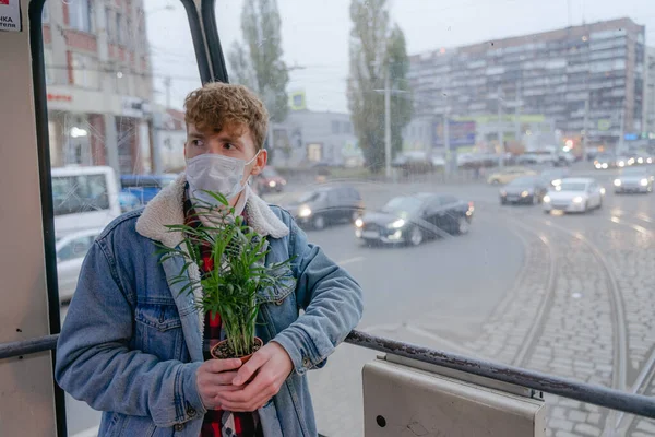 Yüzünde maske, kafasında kıvırcık saçlar, toplu taşıma araçlarında elinde yeşil bir çiçekle, salgın sırasında evine döner.