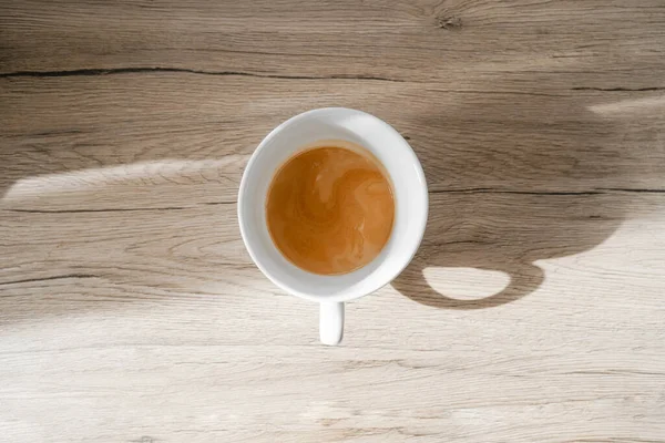Kahve içmenin minimalizmi, beyaz fincanın üzerinde espresso duruyor, üst tarafta, parlak güneş bir fincan kahvenin üzerinde parlıyor.