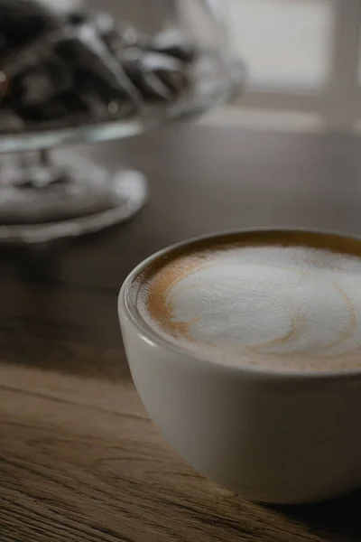 Bir fincan kapuçino masaya yakın duruyor, kahve içeceğine süt köpüğü dökülüyor.
