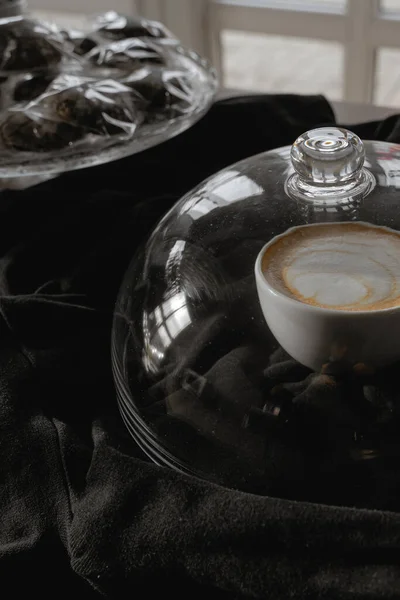 Bir fincan kapuçino, siyah arka planda duran camlarla kaplı.