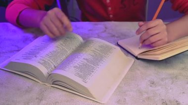 Close up of mixed race teenager doing notes on notebook and reading the christian bible.