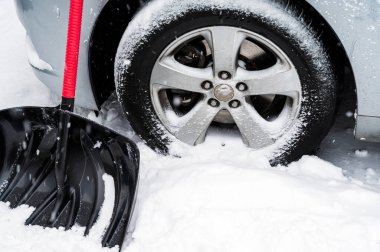 Snow shovel front of car wheel in white snowy day. Winter day routine and problem concept. copy space
