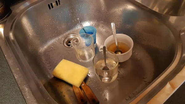 Dirty kitchen sink, with lots of dirty glasses with cups and spoons. Left in time inside the sink.