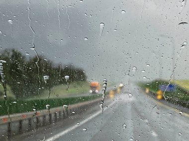 Ön camdan gelen yağmur damlaları, kara bulut, şiddetli yağmur, yol ıslak. Farları açık bir kamyon yaklaşıyor. Yolda görüş mesafesi düşük.