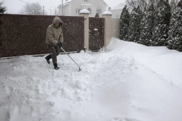 Человек бросает снег с переднего двора собственного дома пластиковой лопатой во время сильного снегопада. — стоковое фото