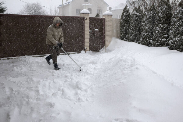 Man throws snow from the front yard of his own house with a plastic shovel during a heavy snowfall.