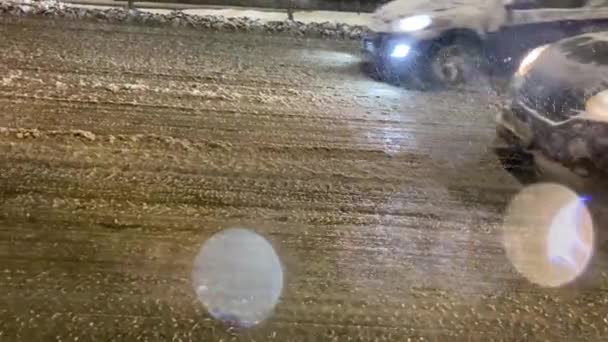 Camino mojado, primer plano, los coches conducen a lo largo de una calle de invierno noche. Nieve con lluvia. Los vehículos conducen por un camino húmedo y resbaladizo con mal tiempo. — Vídeos de Stock