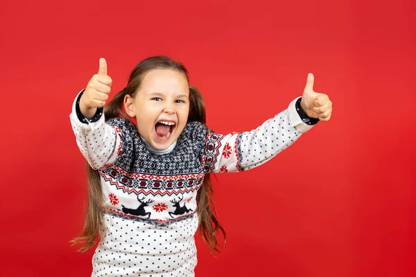 Retrato de risa, chica alegre en suéter blanco de Navidad con renos dando pulgares hacia arriba, aislado sobre fondo rojo — Foto de Stock