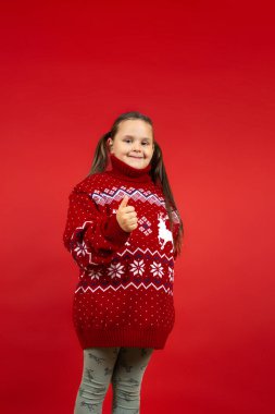 Kırmızı örgü Noel süveteri giyen, geyikli, kırmızı arka planda soyutlanmış, gülümseyen bir kız portresi.