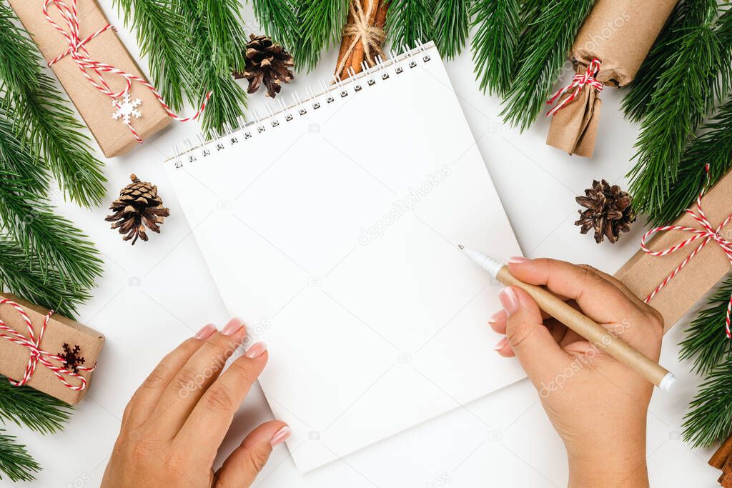 flat lay Christmas frame with decorations, woman hands write letter to Santa Claus on white notebook on white background
