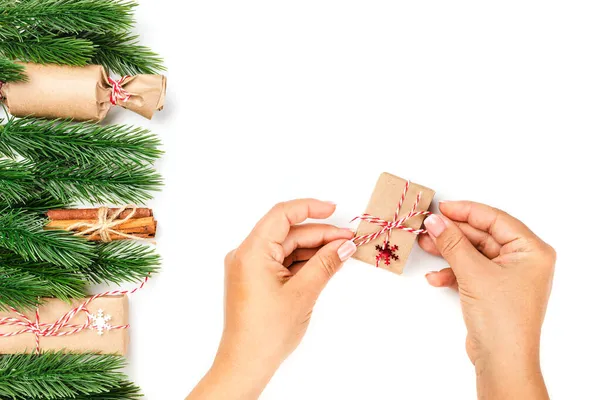 Platte lay van vrouw handen strikken boog van rood touw op geschenkdoos voor kerstgroeten, decor van kerstbomen op witte geïsoleerde achtergrond — Stockfoto