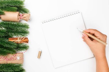 Beyaz masa üzerine el yazması beyaz not defteri ve el yazması kalem, Noel ağacı dalları ve hediye paketleri.