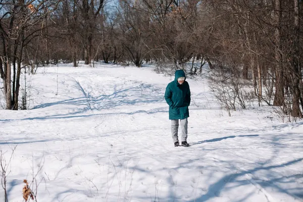 Kaukasische Frauen gehen durch schneebedeckten Wald. Junge Frau in winterwarmer Kleidung genießt Spaziergang auf Winterpfad zwischen hohen Bäumen, Frontansicht — Stockfoto