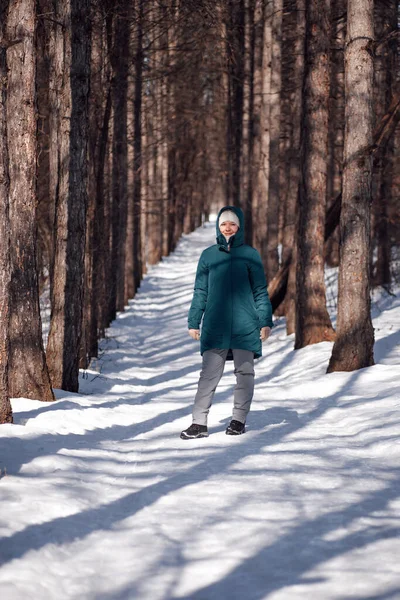 Kaukasische Frau im verschneiten Wald. Junge attraktive Frau in warmer Daunenjacke läuft nach Schneesturm über eine schneebedeckte Landstraße — Stockfoto