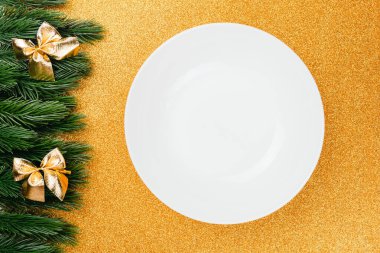 düz yakın plan beyaz tabak üzerinde yatıyordu altın, parlak izole arka plan üzerinde kopya alanı ile köknar dalları ve altın fiyonklar Noel süslemeleri ile