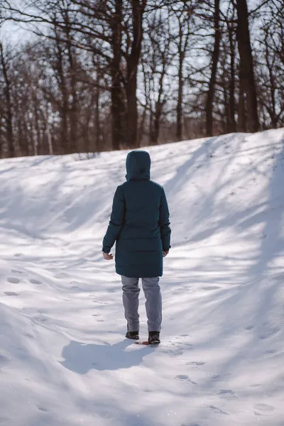 Ung kvinna i grön dunjacka står upp. Vinterväg i skogen täckt med snö, vit kvinna i varma kläder promenader på vackra frostiga soliga dag efter tungt snöfall — Stockfoto