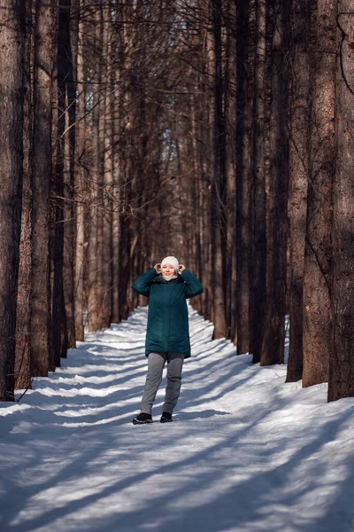 Junge Frau steht auf Straße zwischen Bäumen. Sie hält einen weißen Hut mit den Händen, starker Wind weht und es ist kalt im Wald. — Stockfoto