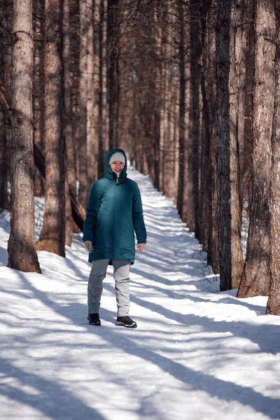 Kaukasische Frau beim Waldspaziergang. Junge attraktive Frau in warmer Daunenjacke steht nach Schneesturm auf schneebedeckter Straße und genießt Sonne an frostigen Tagen — Stockfoto