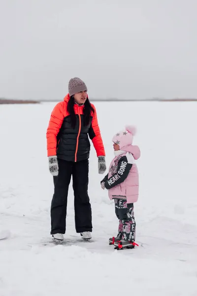 Passeggiata invernale nella natura. Giovane donna e bambina pattinaggio sul fiume congelato, mamma e figlia — Foto Stock