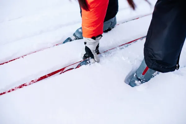 Der Mensch fährt Ski. Nahaufnahme der Beine in grauen Skischuhen auf Skiern, Mann beugt sich nach unten und hebt Ski auf, die auf Schnee liegen — Stockfoto