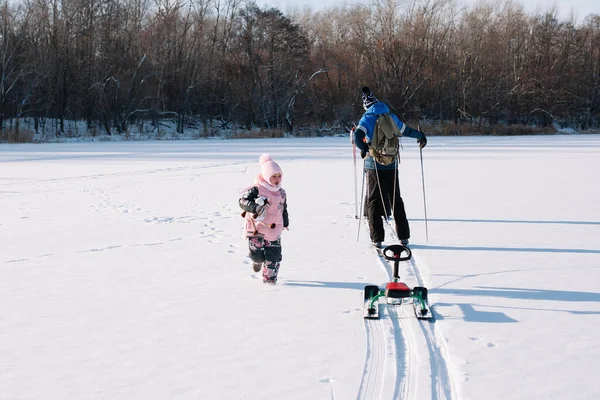 Família em passeio de inverno na floresta. Jovem e criança estão andando na natureza, menina está correndo perto de seu pai, que está esquiando e dirigindo crianças trenó — Fotografia de Stock