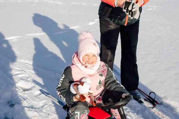 A menina gosta de andar. Criança squints do sol e goza de passeio de trenó através da floresta nevada, sombras na neve — Fotografia de Stock