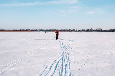 Kayak gezisindeki adam. Kışın eşofmanlı bir adam donmuş gölde kayak yapıyor açık kış gününde, mavi gökyüzü