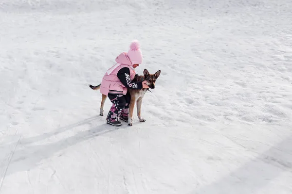 L'enfant joue avec le chien. Petite fille caresse chien rouge et promenades avec elle sur la route enneigée, paysage d'hiver — Photo
