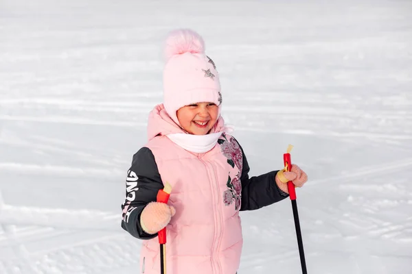 Portret dziecka na śnieżnym tle. Szczęśliwa dziewczynka w różowym ciepłym ubraniu uśmiecha się i uczy jeździć na nartach, zimowy krajobraz — Zdjęcie stockowe