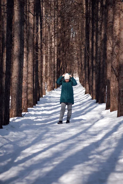 Αγροτικός χειμερινός δρόμος. Νεαρή γυναίκα με ζεστά ρούχα περπατά μέσα στο χιονισμένο δάσος το ηλιόλουστο πρωινό του χειμώνα — Φωτογραφία Αρχείου
