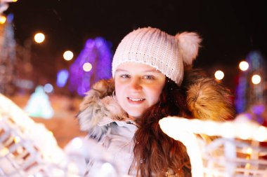 Beyaz örgü şapkalı genç bir kadının yakın plan portresi. Noel süsleri ve arka planda ışıklar. Mutluluk ve eğlence kavramı.