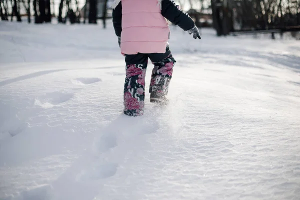 Сліди дітей ніг у снігу. Вид ззаду дитини в теплому зимовому одязі, що йде через снігопад і грає в лісі після сильної сніжної бурі, вид ззаду — стокове фото