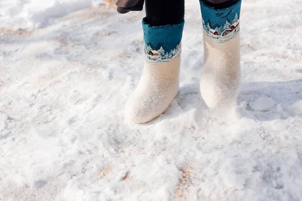 White felt boots with ornament. Close-up of man feet shod in felt boots and standing on fresh snow that fell after heavy snowfall