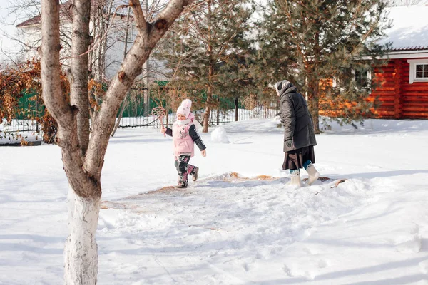 Flickan rengör mattan med traditionella metoder. Barn och kaukasisk kvinna på bakgård på bakgrunden av stugan ren persisk matta med nysnö och mattan slå på vintern — Stockfoto