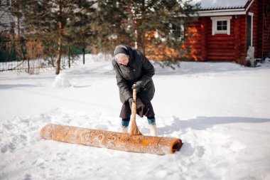 Arka bahçede beyaz bir kadın. Eşarplı ve keçeli çizmeli yaşlı kadın taze kar ve süpürgenin yardımıyla halıyı geleneksel yollarla temizliyor.