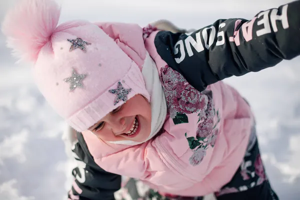Портрет дитини впритул. Маленька дівчинка в рожевій зимовій куртці і капелюсі з помпоном розважається на природі і насолоджується сонячною погодою і грає зі снігом на морозному зимовому ранку — стокове фото