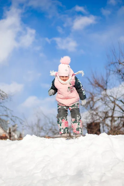 Paesaggio invernale con cielo blu. Bambino in tuta invernale calda si sta divertendo, giocando e pescando in cumulo di neve, cavalcando scivolo di neve durante la passeggiata nella natura nella soleggiata giornata invernale — Foto Stock