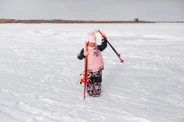 Criança posa no fundo da paisagem de inverno. Menina aprende a esquiar, ela fica na estrada nevada após a tempestade de neve e sorri — Fotografia de Stock