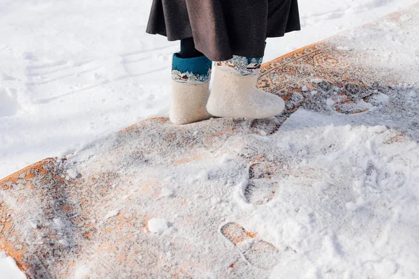 Покриття килима в снігу. Чищення пилового килима зі східною текстурою на вулиці взимку, традиція прибирання килимів, чоловік у відчутних чоботах, що стоять у снігу. — стокове фото