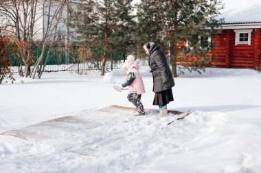 Aile arka bahçede halı temizliyor. Beyaz kadın ve çocuk geleneksel olarak temiz halı, kışın ahşap kulübenin yanında taze kar ve halı çırpıcı.