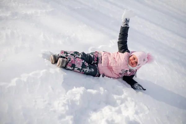 Дитина грає зі снігом. Маленька дівчинка насолоджується прогулянкою на природі, розважається і катається на снігових гірках без санки в сонячний зимовий день — стокове фото