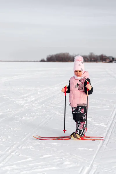 A criança aprende a esquiar. Menina em rosa terno esqui no dia gelado no fundo da floresta de inverno, vista lateral, fundo de neve — Fotografia de Stock