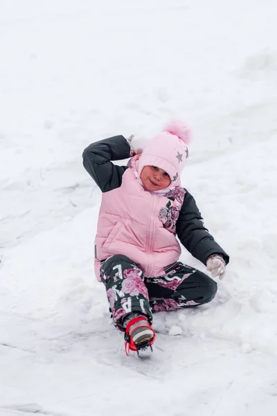 Το παιδί παίζει χιονόμπαλες. Ευτυχισμένο κοριτσάκι με ζεστό κοστούμι κάθεται σε χιονισμένο δρόμο και απολαμβάνοντας την ξεκούραση στη φύση — Φωτογραφία Αρχείου