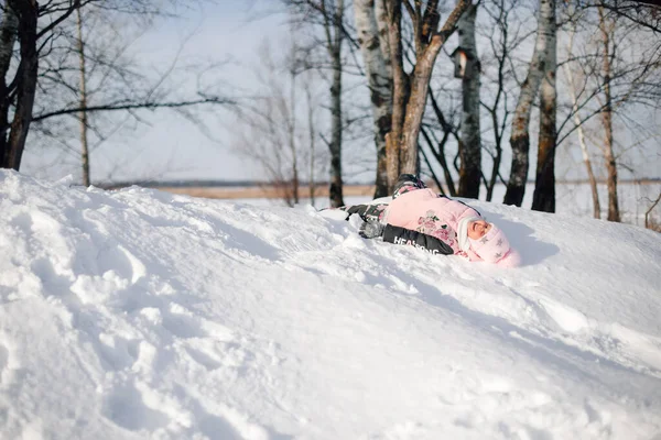 Enfant monte sur glissade de neige. Fille aime la promenade hivernale dans la nature en forêt, s'amuse, joue et se couche sur la neige — Photo