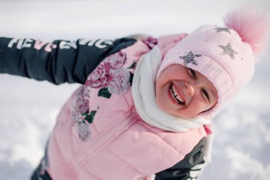 Gülümseyen çocuğun portresi. Pembe şapkalı küçük bir kızın soğuk kış sabahında yürüyüş yaparken karla oynuyor ve güneşin tadını çıkarıyor.